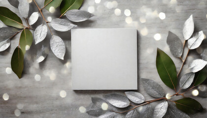 Top view of a blank white sheet of paper on a silver background surrounded by silver leaves