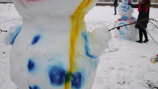 Painted snowman on playground and woman painting near another one.