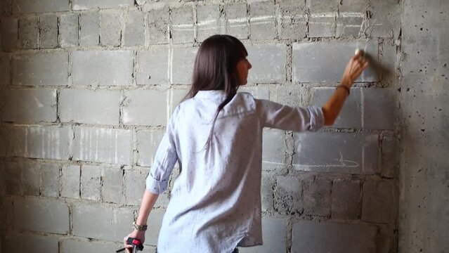 Woman drawing rectangle of future TV on wall of flat without finishing.