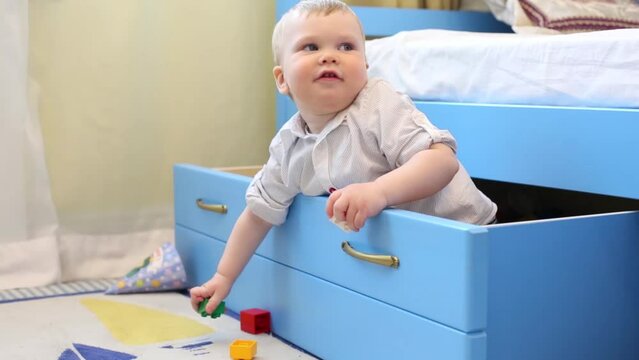 Little boy plays toys and sits in big drawer in room