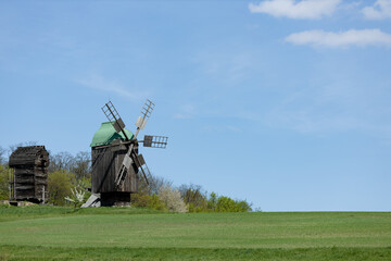 Fototapeta premium Rustic Windmill Amidst Green Fields Under Blue Sky
