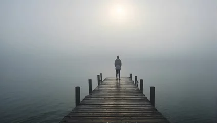  Person standing alone on a foggy pier, looking out at the sea, shrouded in mist, 4k. generative AI © Zohaib