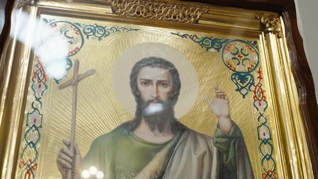 Iconic painting of Jesus Christ holding a cross, with a gilded halo, intricate border designs, and religious symbols, set within an ornate golden frame, reflecting rich Christian iconography