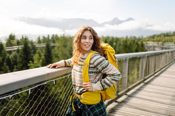 Young woman traveler walking across bridge in the middle of a forest. Travel and active lifestyle concept.