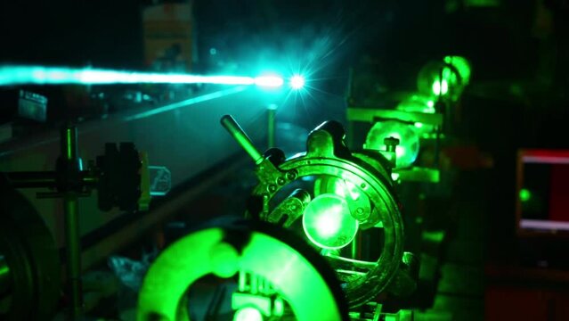 Green laser in optic assembly and bright blue laser above in dark close up.