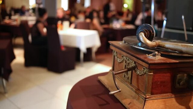 Old gramophone (focus on it) with reproducer and plate and people 