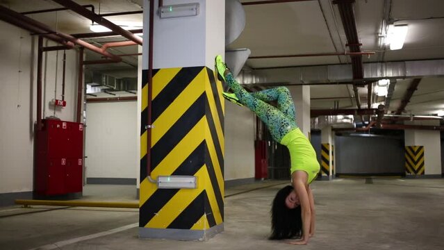 Young girl gets on her hands and doing stretching in indoor parking