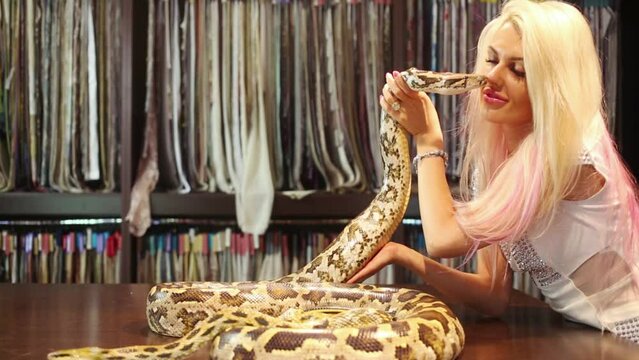 woman holding snake lying on table and touching it with lips near small snake