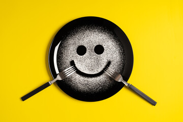 Smiling face, concept made with plate and flour, yellow background, star shaped eyes, black plate,...