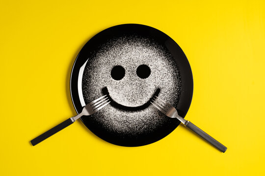 Smiling face, concept made with plate and flour, yellow background, star shaped eyes, black plate, happy mood, facial expressions, forks in the shape of arms with different positions