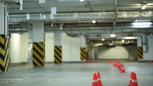 Guy on roller skates jumping four orange cones on underground parking.