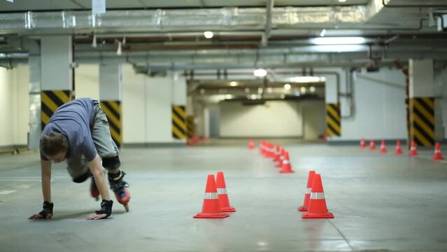 Man on roller skates taking run, jumping and falling near cones on parking.