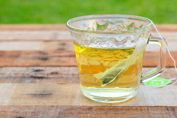 Transparent glass cup with a light colored tea bag on a wooden base and green background