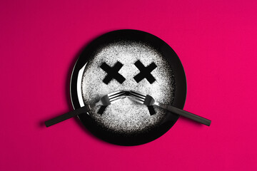 Sad face, concept made with plate and flour, majenta background, x-shaped eyes, black plate, happy mood, facial expressions, forks in the shape of arms with different positions