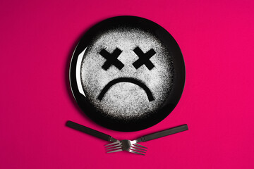 Sad face, concept made with plate and flour, majenta background, x-shaped eyes, black plate, happy mood, facial expressions, forks in the shape of arms with different positions