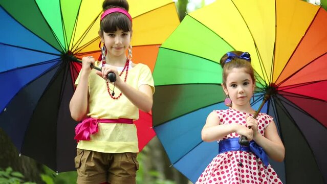 Two girl with umbrellas turning them, looking to each other and smiling.
