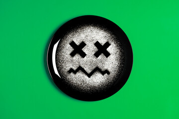 Sad face, face I don't like, concept made with plate and flour, green background, x-shaped eyes, black plate, sad mood, facial expressions
