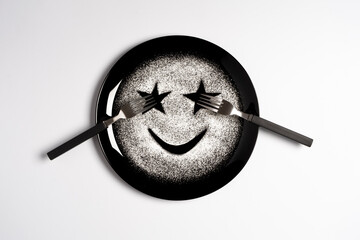Smiling face, concept made with plate and flour, white background, star shaped eyes, black plate, happy mood, facial expressions, forks in the shape of arms with different positions