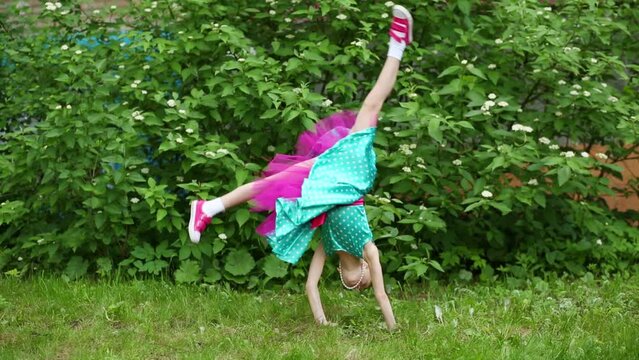 Girl in colored spotted dress doing cartwheel side and back on grass