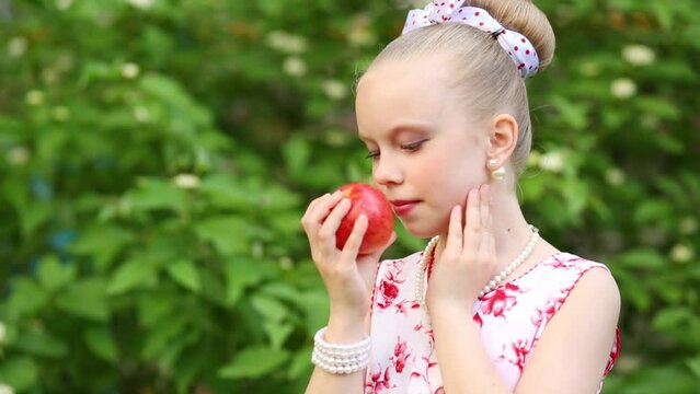 Girl looking up and smelling apple in hand beads near bushes.