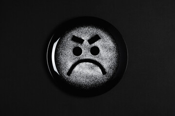 Displeased face, frowning eyebrows, concept made with plate and flour, black background, black plate, sad mood, facial expressions