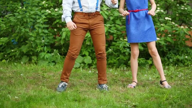Legs of boy and girl in blue dress dancing on green grass.