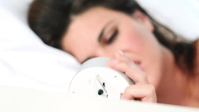 Clock, wake up and tired or exhausted woman in bedroom of home with alarm ringing on Monday morning. Time, relax and sleeping with angry or annoyed young person lying alone in bed of apartment