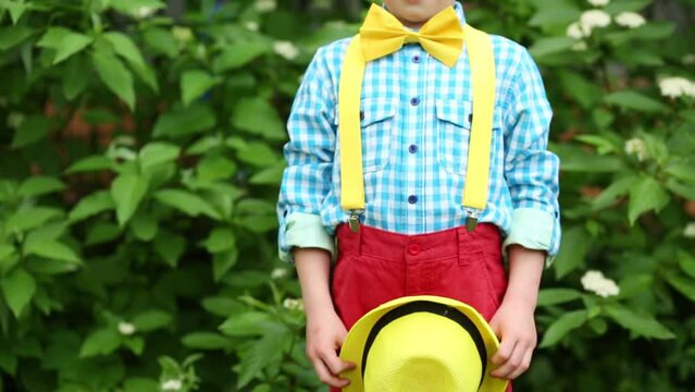 hat in hands of boy in red trousers, checkered shirt and yellow bow tie