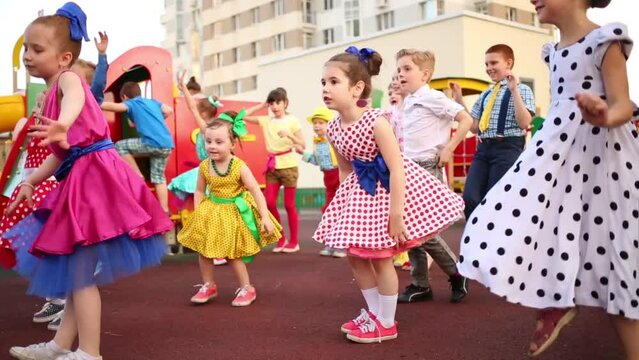 Fourteen small girls and boys in multi-color clothes jumping with raised hands
