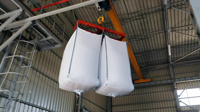 Industrial Bulk Bags Suspended in Warehouse, White, large bulk bags filled with materials, hanging in an industrial warehouse.