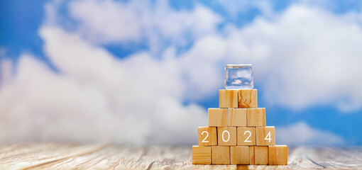 Wooden blocks in a tower with an ice cube on top, climate change icons, and the year 2024. Concept...