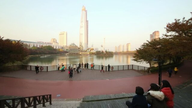 People sitting and walking on waterside pond opposite entertainment park