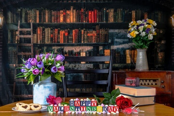 Happy Valentines day spelled in wood blocks with candy conversation hearts lollipops and spring flowers in old library - obrazy, fototapety, plakaty