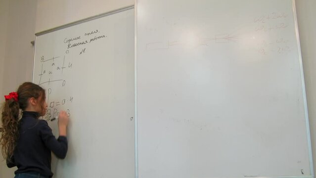 Young girl writes schema and formulas on whiteboard before teacher