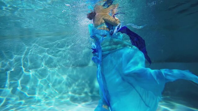 Woman in blue dress poses deep in water during photo session. Timelapse