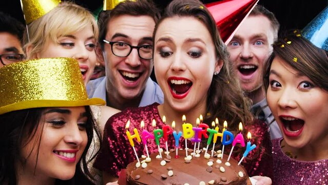 Group, celebration and candles on cake for birthday, party and happiness at event with slow motion. Happy, surprise and people with shock on face with dessert for friends and community together