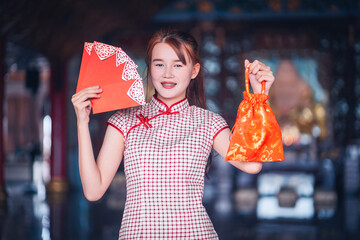 Portrait Asian beautiful woman wearing a cheongsam smiling and holding red envelopes fan, show Red...