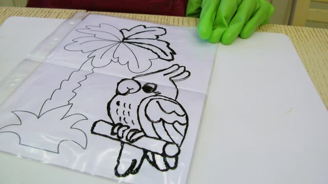 Kid in green gloves draws by transparent surface above picture.