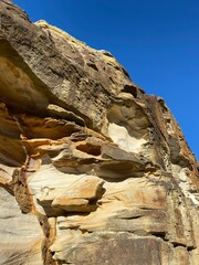 Rock formation under a blue sky. Ochre and brown rock undulating in the sun. Cliff, mineral kingdom on the coast. Wind-sculpted ore. Coastal landscape. Canyon geology.