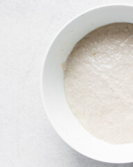 High hydration bread dough resting in a white bowl, Top view of wet dough rising in a mixing bowl, bread dough in a white ceramic mixing bowl