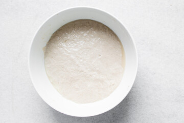 High hydration bread dough resting in a white bowl, Top view of wet dough rising in a mixing bowl,...