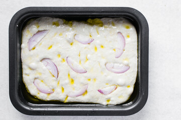 onion focaccia dough in a baking tin, Flatlay of focaccia with olive oil red onion topping, fresh homemade focaccia bread on white marble countertop