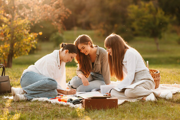 Ecstatic young female students are learning together while sitting in park on a blanket.