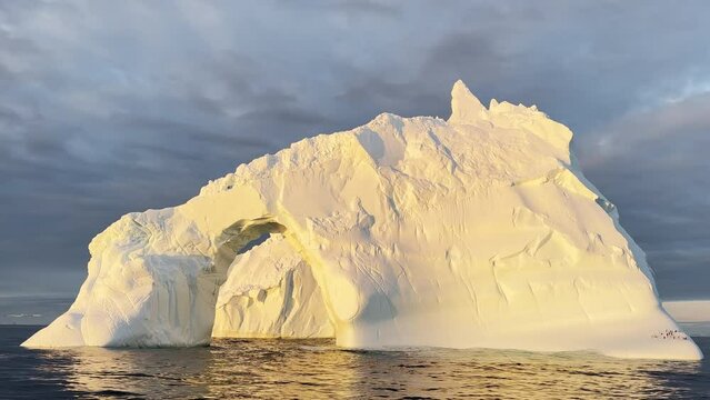 Arch in a huge iceberg, high breakaway glacier drifts in the southern ocean off the coast of Antarctica at sunset, the Antarctic Peninsula, the Southern Arctic Circle, azure water, cloudy weather