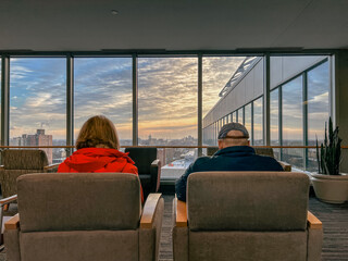 Rear view of a senior couple in a waiting area. They are sitting in comfortable chairs. Large...