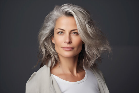 Studio portrait of a mature woman with silver hair and a white shirt, confidence and timeless elegance, isolated on gray background