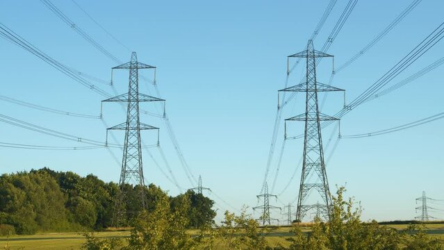 High voltage transmission line near a power station in the English countryside. Industrial construction with numerous steel towers and cables for distribution of electric energy along large distances.