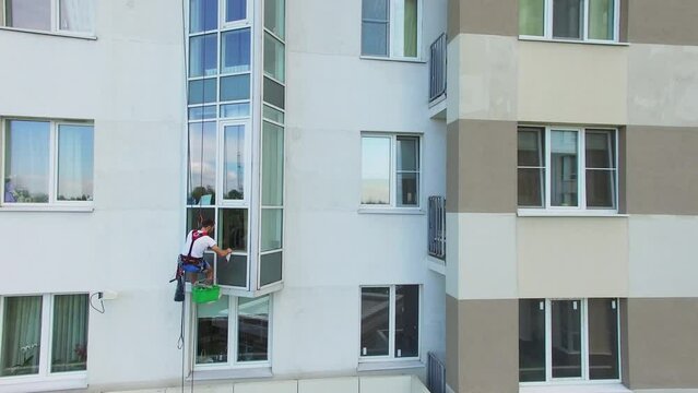 Man hangs on rope and cleans window of tall residential house