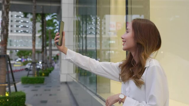 Smiling young lady taking a selfie with her cell phone in the city, showcasing her trendy style and accessories. Happy woman using mobile technology for personal branding and social media.