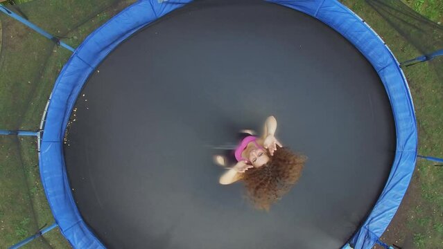 Woman jumps in sports clothes on round trampoline. Aerial view